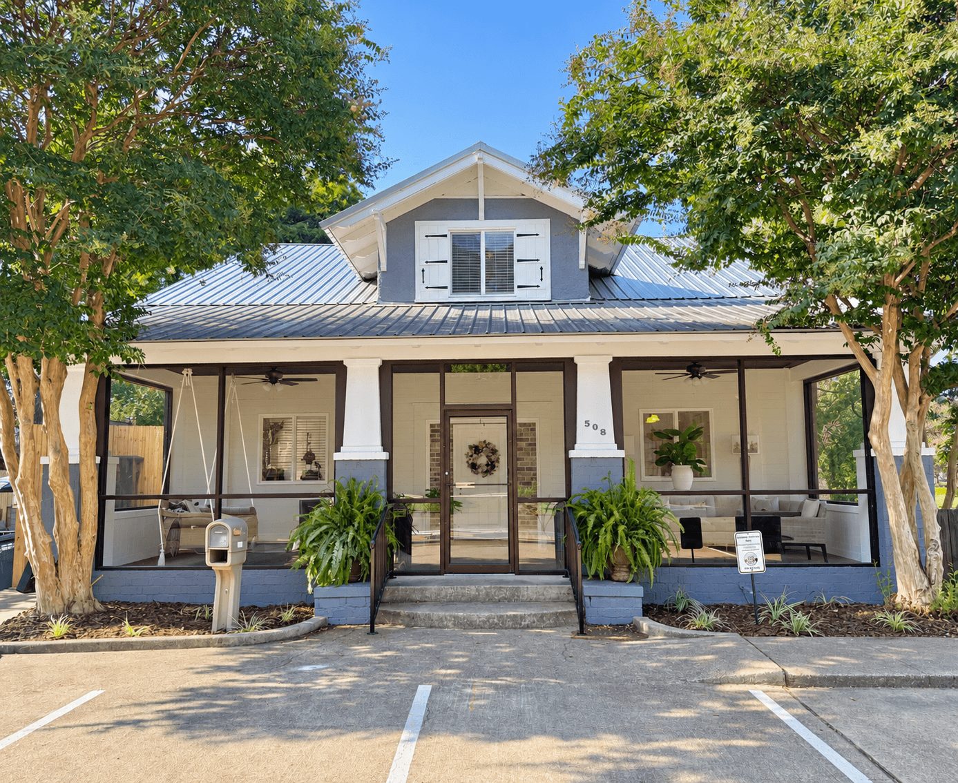 The Dooey House: a historic home with a deep screened front porch, white columns and crape myrtles on either side