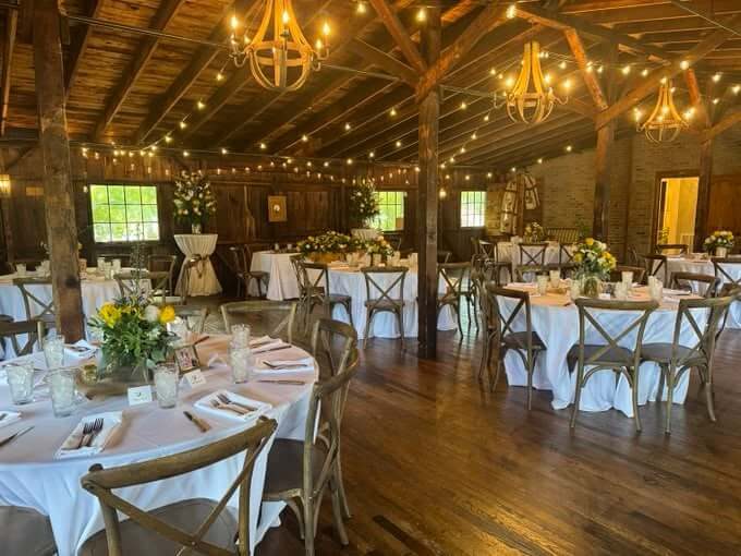 Fellowship Place set for a dinner: round tables with white linens under chandeliers and string lights