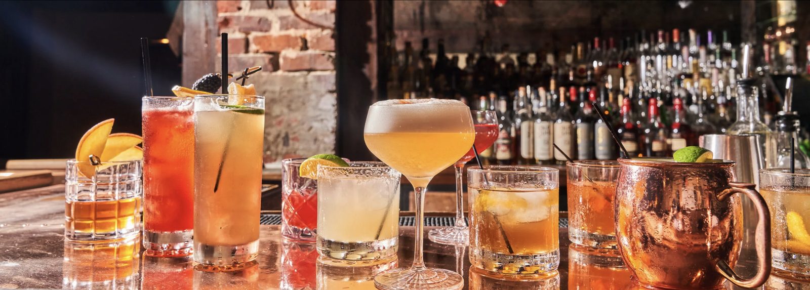 A row of cocktails on The Guest Room's bar, with shelves of spirits behind