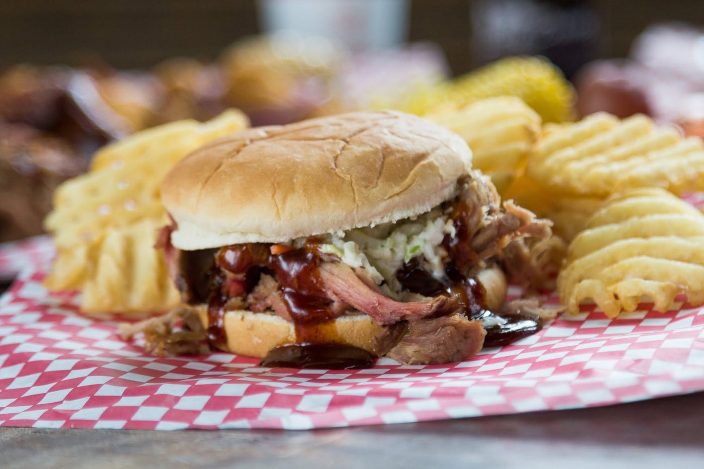 A pulled pork sandwich with barbecue sauce and slaw, waffle fries on the side